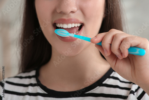 Woman brushing her teeth with plastic toothbrush indoors, closeup