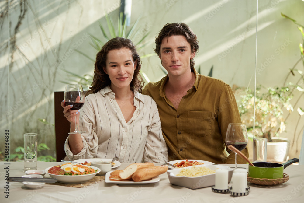 Portrait of smiling boyfriend and girlfriend sitting at dinner table with delicious homemade dishes