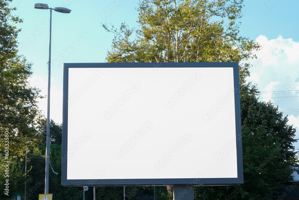 Blank advertising sign board display billboard mockup outside with trees and blue cloudy sky background. White billboard banner background in city. Selective focus of billboard. Blank advertising sign board display billboard mockup outside with trees and blue cloudy sky background. White billboard banner background in city. Selective focus of billboard.