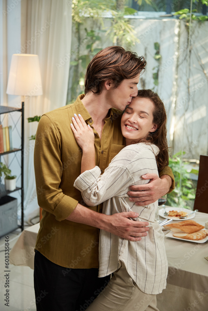 Happy young man hugging girlfriend and kissing her of forehead