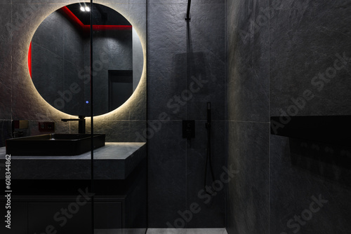 interior design of the bathroom in a modern version of dark tiles and lighting with a round mirror