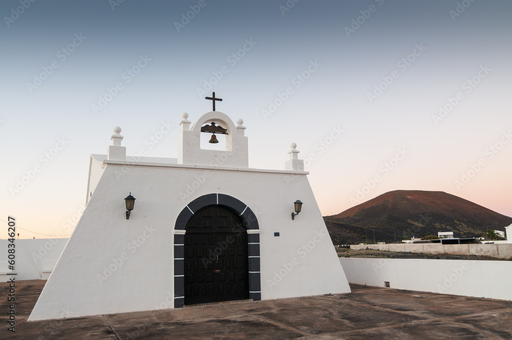 Paisaje de Lanzarote, islas canarias,  con una ermita blanca y un volcán al fondo.
