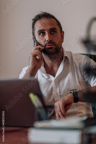 A businessman talking on his smartphone while seated in an office, showcasing his professional demeanor and active communication.