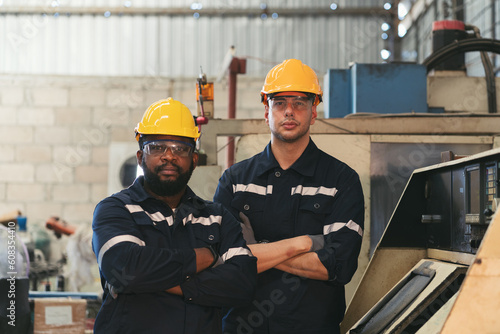 Portrait of two male engineer worker standing at work  in industrial factory, wearing safety uniform, glasses and hard hat. Two male technician in workshop