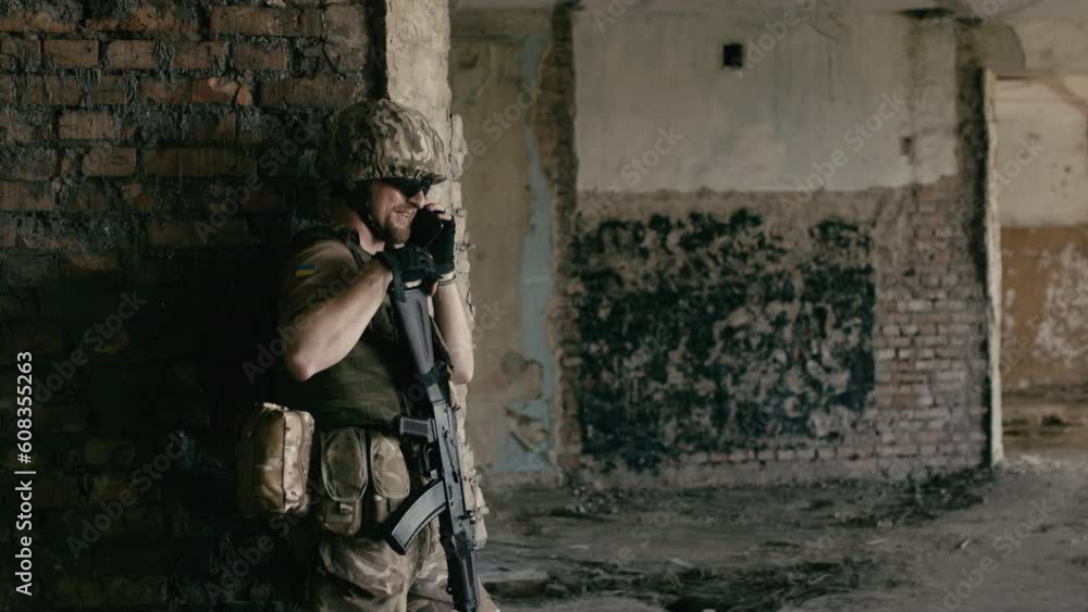 A military man stands in a building after a fight and talks on a smartphone with his mother or girlfriend. Satisfied military man talking on the phone in his spare time A military man stands in a building after a fight and talks on a smartphone with his mother or girlfriend. Satisfied military man talking on the phone in his spare time
