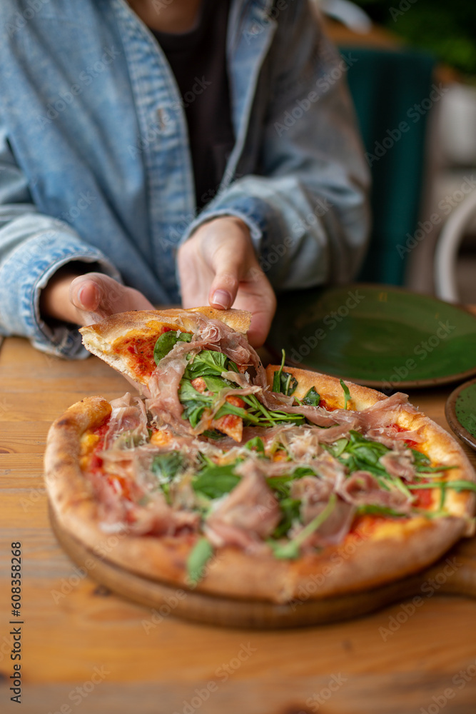 woman eating pizza with ham and spinach on wooden table