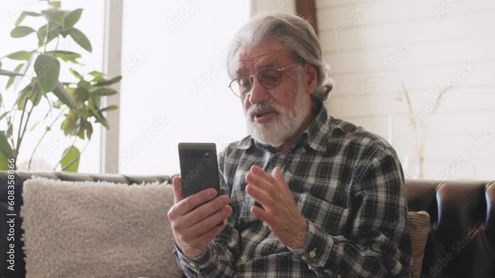 Senior man looking at the phone screen during video call. Grandfather in glasses and checkered shirt talking on the phone Senior man looking at the phone screen during video call. Grandfather in glasses and checkered shirt talking on the phone