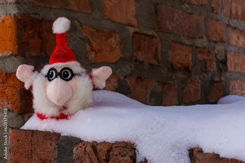 Small pretty toy Santa sitting on a snowy old brick house in winter. Copy space. Selective focus.