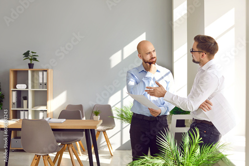 Two business men standing in office near the workplace discussing making successful deal or signing contract. Company employees talking and making great decisions with brainstorming on a meeting. © Studio Romantic