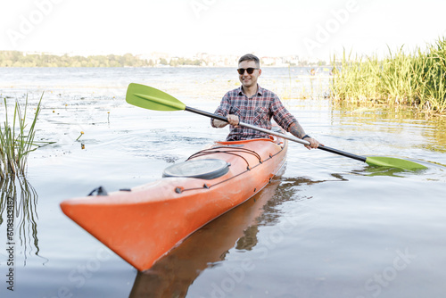 A young Caucasian man sits in a kayak and paddles. The concept of water entertainment.