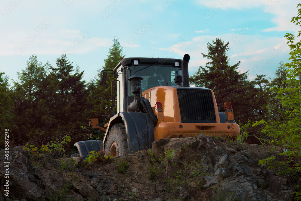 Orange backhoe excavator at the construction site with rock and trees