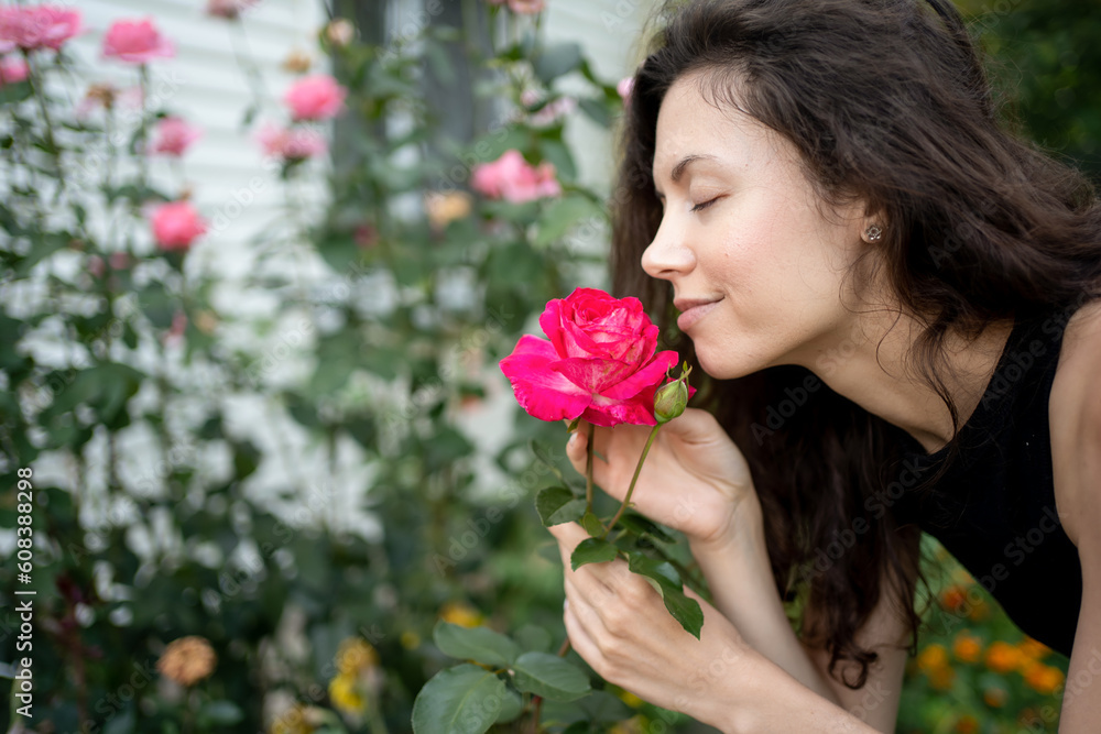 Fototapeta premium pretty brunette female smelling bloom roses and enjoying in garden outdoors