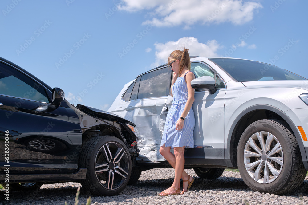 Sad young woman driver standing near her smashed car looking shocked on crashed vehicles in road accident Sad young woman driver standing near her smashed car looking shocked on crashed vehicles in road accident