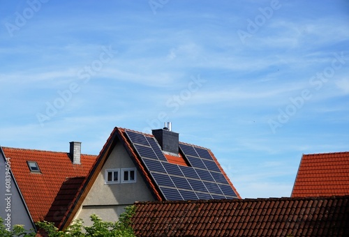 Dächer von alten kleinen Häusern mit roten Dachziegeln und blauen Solarpanels in Kleinstadt vor Himmel bei Sonne am Abend im Frühling