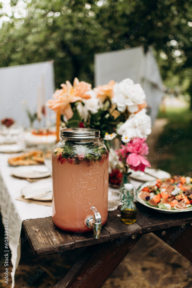 glass jar with strawberry lemonade on a wooden party table. picnic party outdoors. details of a decorated table for a party. glass jar with strawberry lemonade on a wooden party table. picnic party outdoors. details of a decorated table for a party.