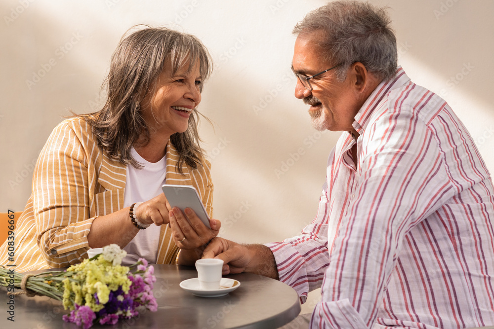 Happy old woman show phone to man in casual, sit at cafe table, enjoy date together Happy old woman show phone to man in casual, sit at cafe table, enjoy date together