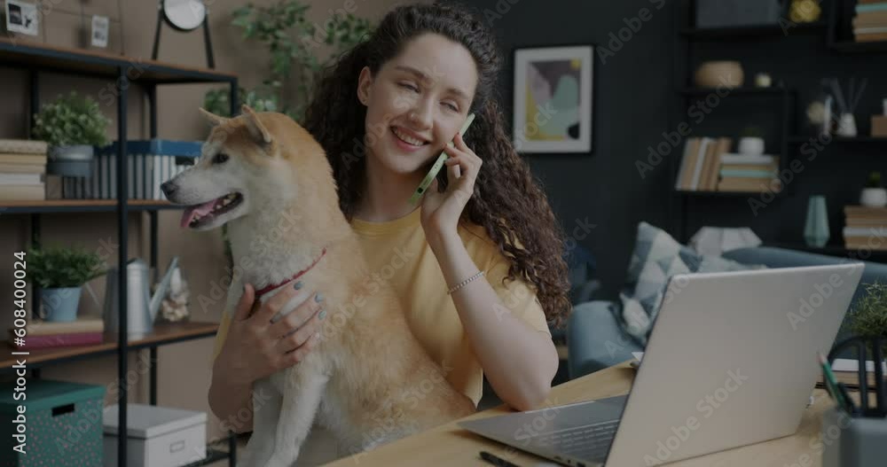 Young woman freelancer talking on mobile phone and hugging cute shiba inu dog in workplace in apartment. Domestic animals and freelance work concept. Young woman freelancer talking on mobile phone and hugging cute shiba inu dog in workplace in apartment. Domestic animals and freelance work concept.