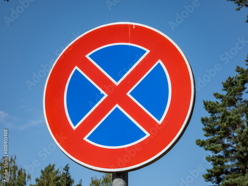 Metal signwith a red circle and red cross over a blue background outdoors. A sign indicates a clearway and means a parking prohibition