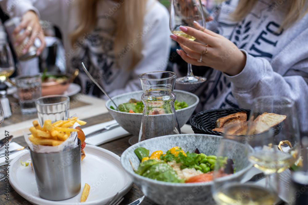 Meals on restaurant table in Paris. Female friends spend time eating salads and french fries, drinking white wine.