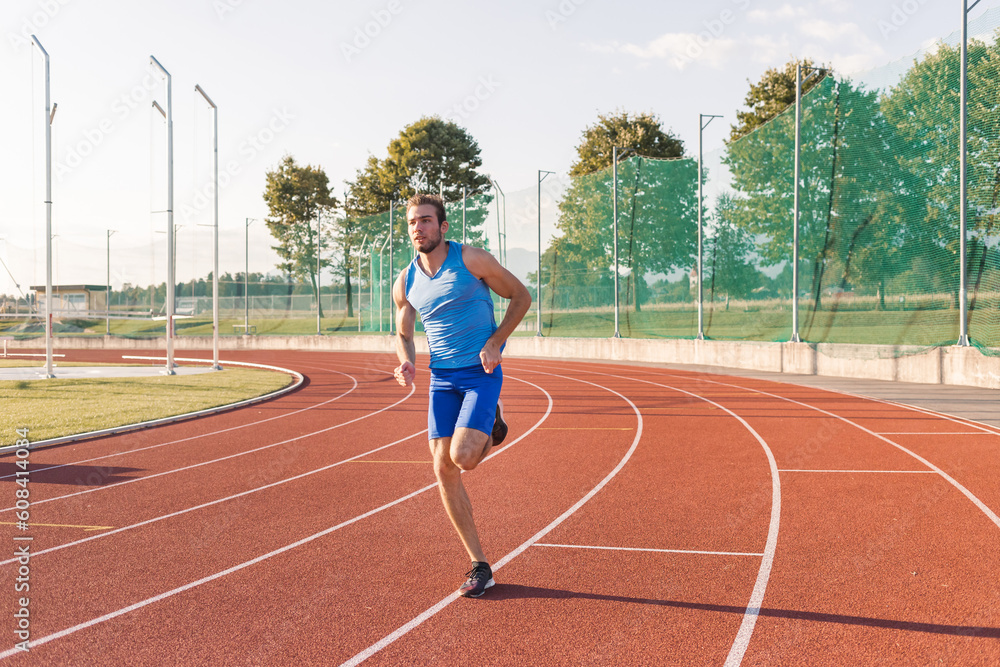 Young man, a professional athlete with a serious and focused face running along an outdoor athletic track near the sports field Young man, a professional athlete with a serious and focused face running along an outdoor athletic track near the sports field