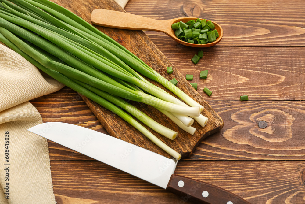 Board with fresh green onion on wooden background