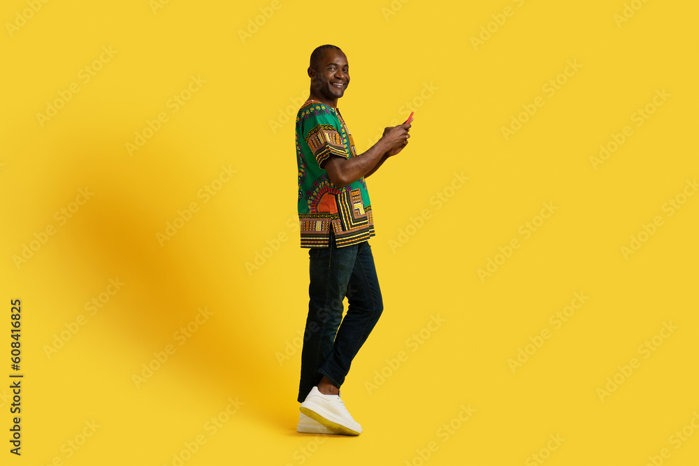 Happy middle aged black man using smartphone on yellow