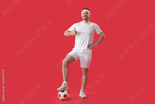 Fototapeta Naklejka Na Ścianę i Meble -  Happy man with soccer ball showing thumb-up on red background