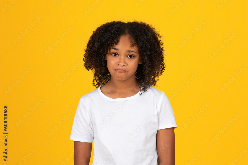 Sad upset teen curly african american girl in white t-shirt looking at camera, isolated yellow studio background Sad upset teen curly african american girl in white t-shirt looking at camera, isolated yellow studio background
