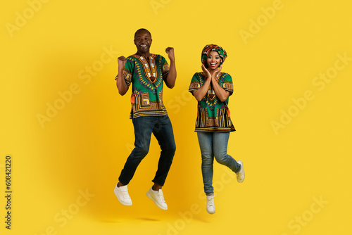 Thrilled african couple jumping up and gesturing on yellow