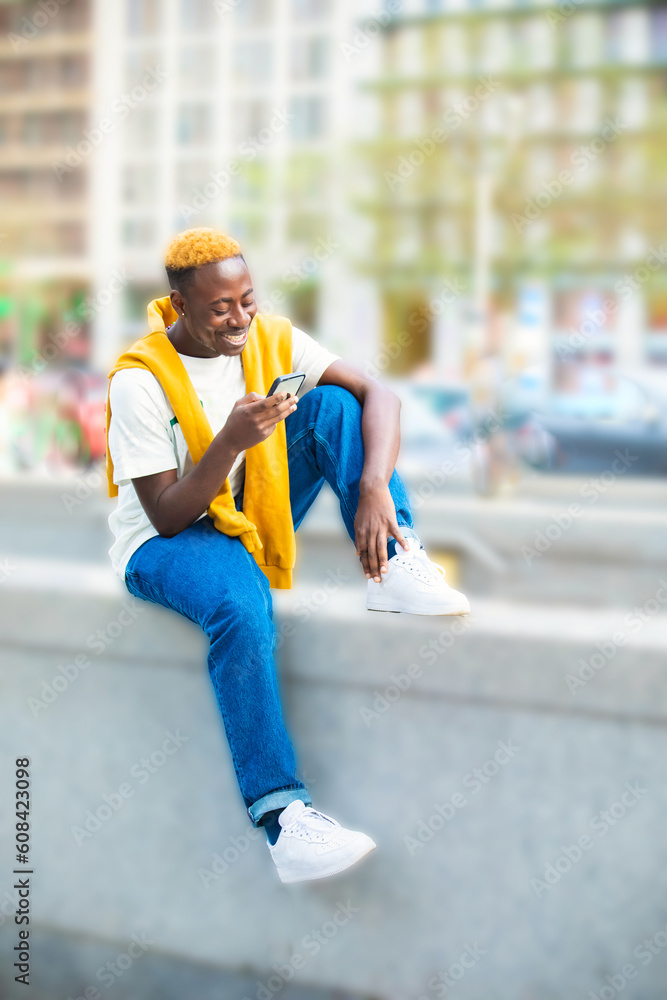Emotional young black guy in yellow casual raising with smartphone Emotional young black guy in yellow casual raising with smartphone