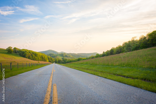 Obraz na płótnie Paved road through rural grassy fields and mountain ranges at sunset