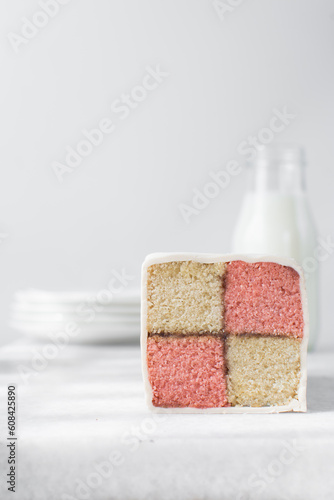 Battenburg cake on a white tray, almond and strawberry sponge cake covered in white fondant, pink and yellow check cake