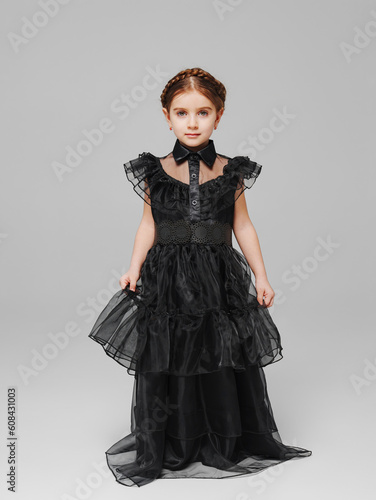 cute little girl with pigtail in a black long curvy dress on a gray background. 