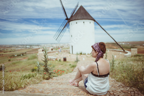 Woman sitting in front of a traditional windmill, Don Quixote's Windmills, Molinos de Viento de Consuegra, Consuegra, Toledo, Castilla la Mancha, Spain photo