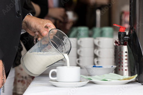 Frau füllt am Buffet Milch aus einer Karaffe in eine Kaffeetasse