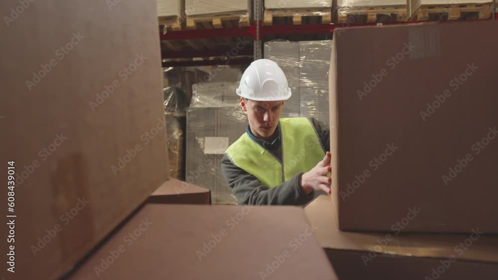 Young Caucasian male loader checking and moving cardboard box while working at warehouse Young Caucasian male loader checking and moving cardboard box while working at warehouse