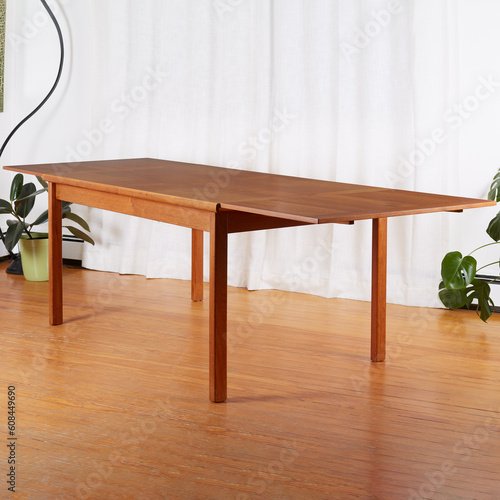 Mid-century modern teak draw leaf table. Interior scene photograph of luxury furniture. Houseplants and white curtain in the background.