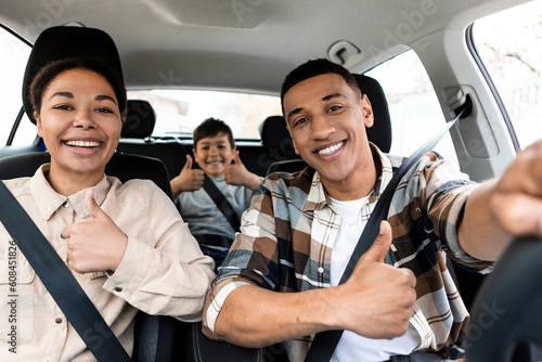 Canvas Print Happy african american family of three driving new car and gesturing thumbs up,