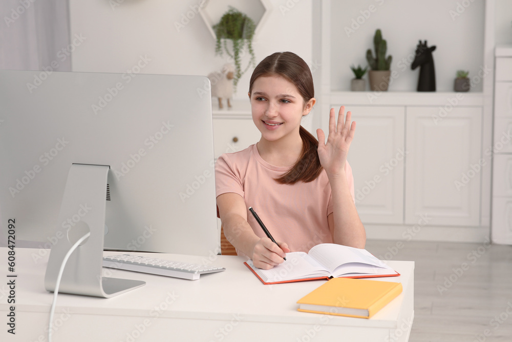 Cute girl writing in notepad while using computer at desk in room. Home workplace Cute girl writing in notepad while using computer at desk in room. Home workplace