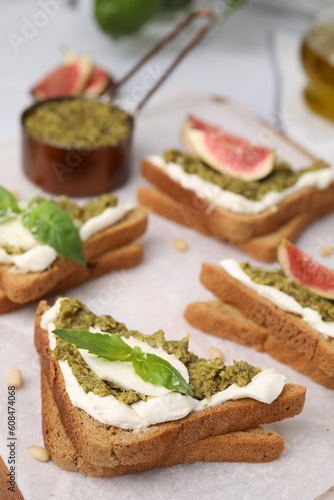 Tasty bruschetta with cream cheese, pesto sauce and fresh basil on parchment paper, closeup