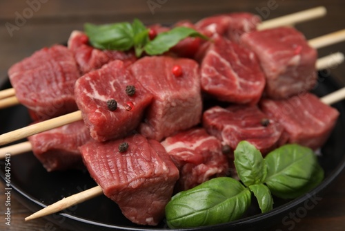 Wooden skewers with cut fresh beef meat, basil leaves and spices on table, closeup