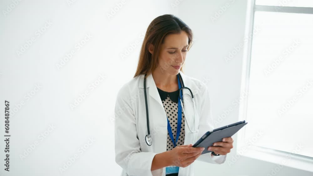 Portrait of female doctor wearing white coat walking into focus looking at patient notes on digital tablet on hospital stairs - shot in slow motion Portrait of female doctor wearing white coat walking into focus looking at patient notes on digital tablet on hospital stairs - shot in slow motion