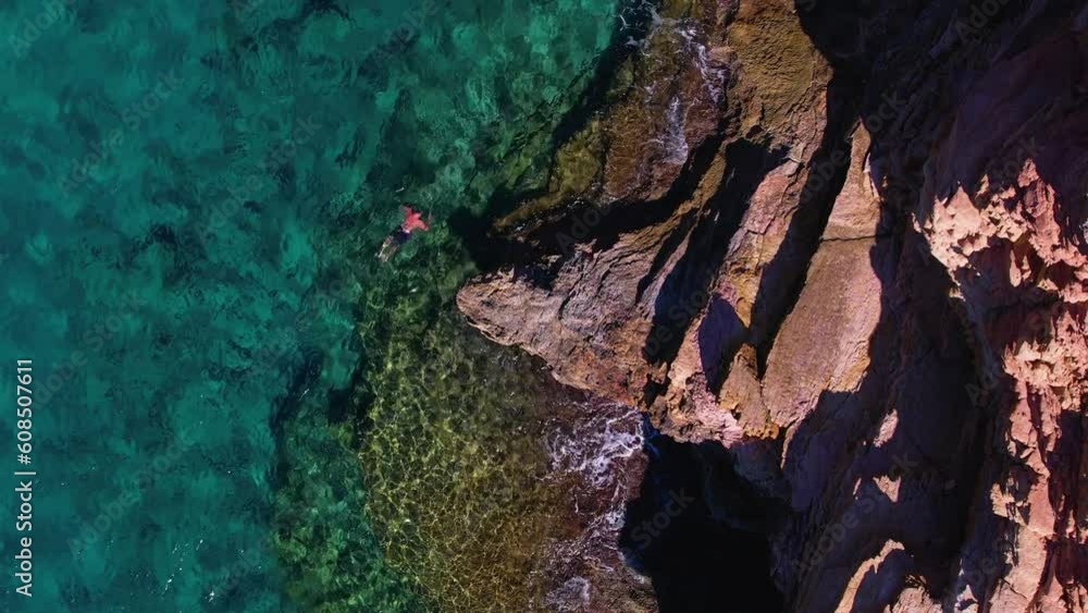 Top down view of a person swimming in the sea next to the rocks Top down view of a person swimming in the sea next to the rocks