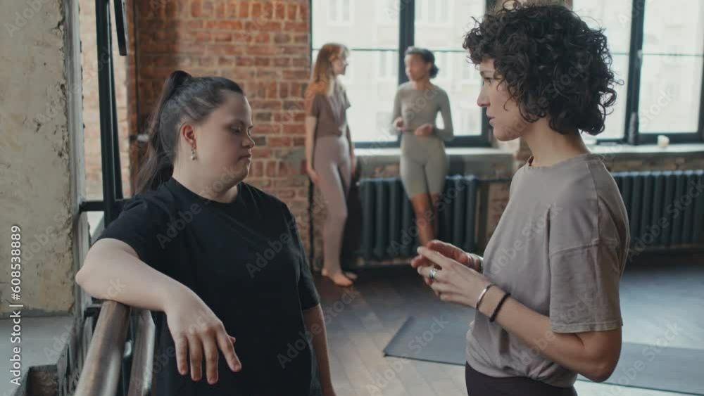 Caucasian woman with curly hair having conversation with her friend with Down syndrome after yoga workout Caucasian woman with curly hair having conversation with her friend with Down syndrome after yoga workout