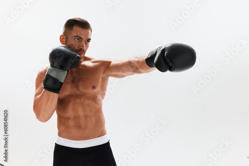 Man athletic bodybuilder poses in boxing gloves with nude torso abs in full-length background, boxing and martial arts. Advertising, sports, active lifestyle, competition, challenge concept.  © SHOTPRIME STUDIO