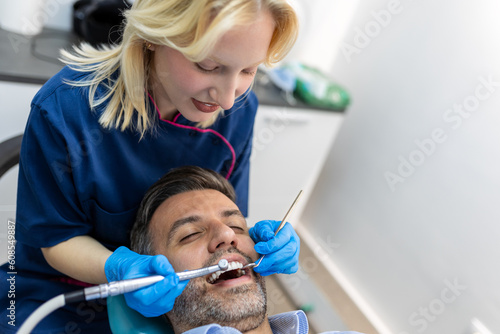 Young female dentist examining teeth of her patient during appointment at dental clinic. Hands of a doctor holding dental instruments near patient s mouth. Healthy teeth and medicine concept