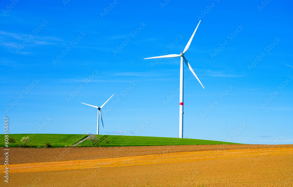 Windmill against a blue sky and with a field in the foreground. Energy generation through wind power.


