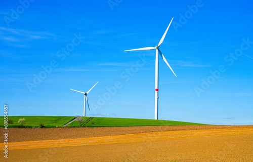 Windmill against a blue sky and with a field in the foreground. Energy generation through wind power.