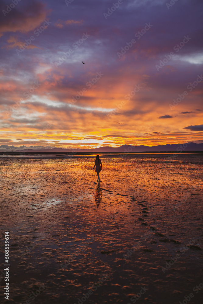 Vertical shot of a female model walking on a beach in front of a mesmerizing view of the sky and clouds