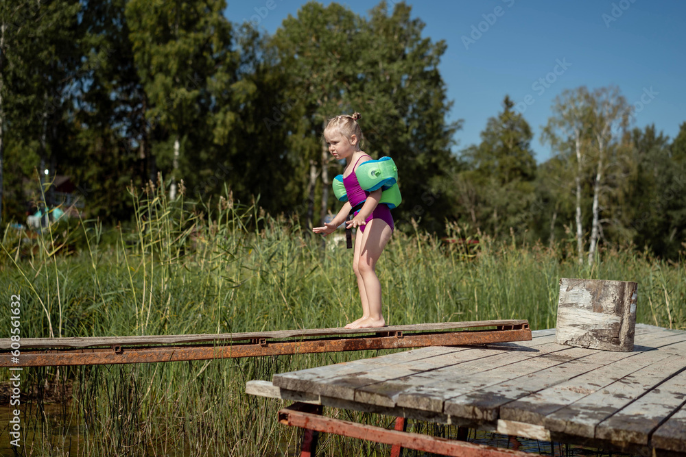 cute little caucasian blond girl walking along plank on pier over the pond